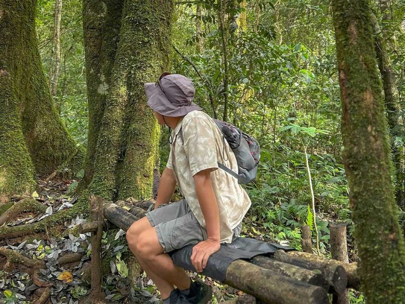 Traveller resting on a forest bench during a Langbiang Mountain trekking tour, surrounded by mossy trees and jungle scenery near Dalat.