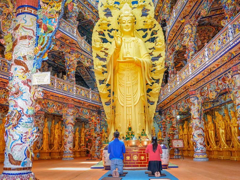 Visitors praying in front of the large Buddha statue at Linh Phuoc Pagoda in Dalat, highlighting the spiritual atmosphere of the temple
