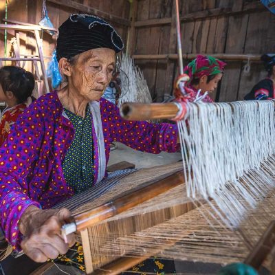 An elderly ethnic woman weaving fabric using traditional methods in Lung Tam Village, Ha Giang.