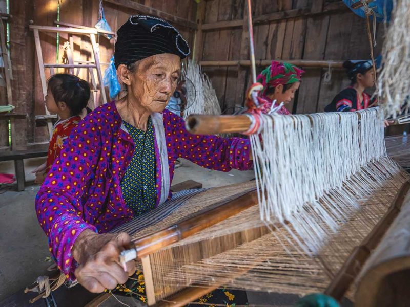 An elderly ethnic woman weaving fabric using traditional methods in Lung Tam Village, Ha Giang.