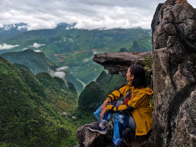 A girl sitting next to an overhanging rock, which is a popular photo stop along the Ma Pi Leng Skywalk