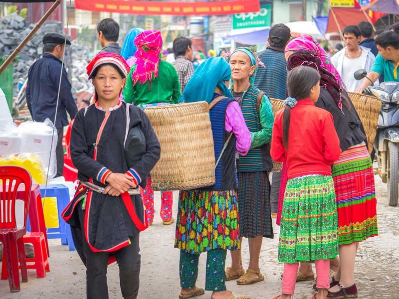 A group of ethnic women in colorful traditional clothing chatting at Meo Vac Market.