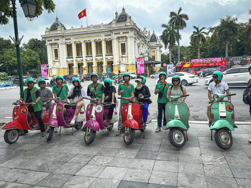 Travelers and local Vespa guides posing in front of Hanoi Opera House before a motorbike tour