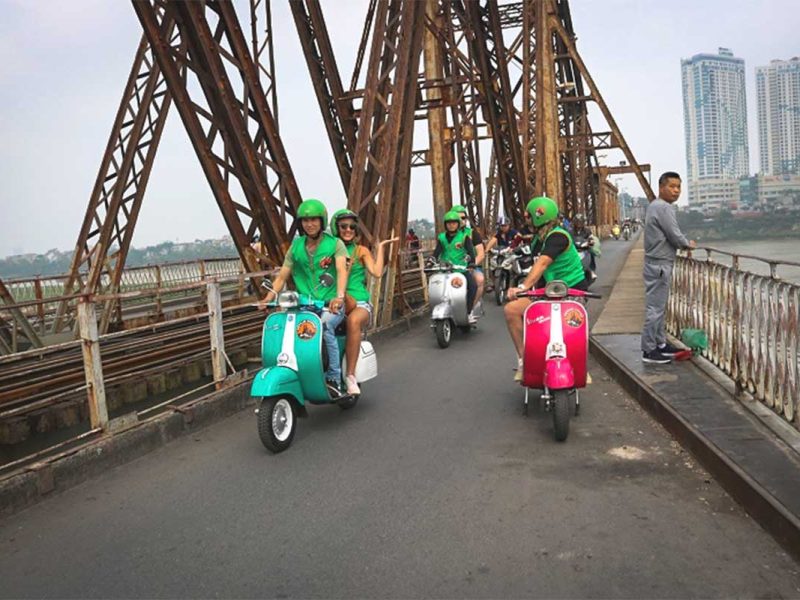 Vespa motorbike tour group crossing Long Bien Bridge with local guides in Hanoi