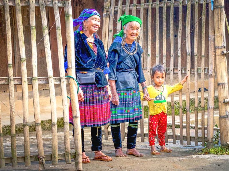 Two colorful ethnic elderly woman wearing traditional clothes and a young child in front of a local house in Mu Cang Chai