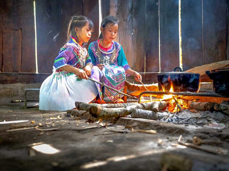 Ethnic minority children in Mu Cang Chai cooking over an open fire inside a traditional house