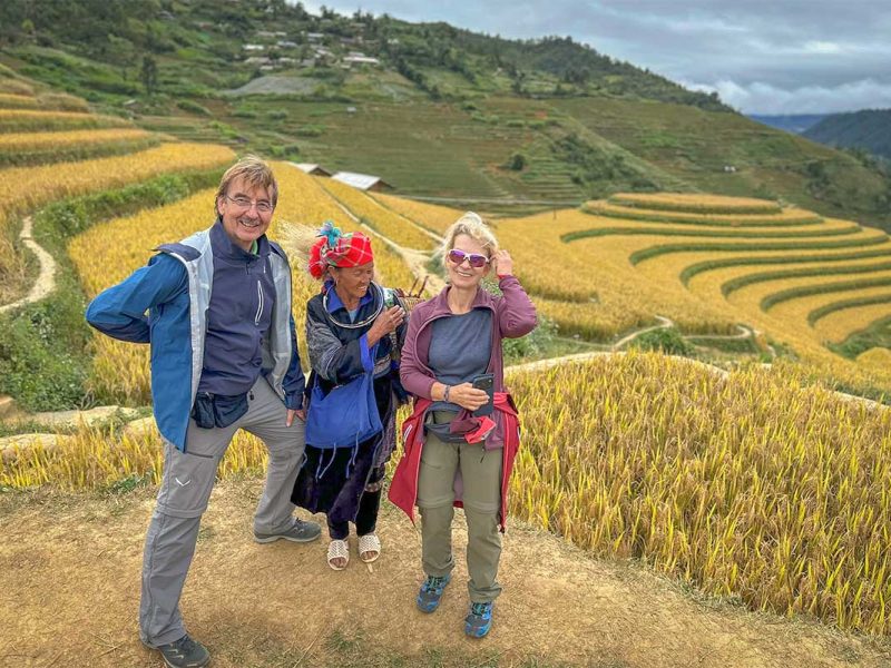 Local Vietnam guests with a local Hmong woman on Raspberry Hill in Mu Cang Chai, standing among golden rice terraces during harvest season and showing genuine interaction on a guided trekking experience.