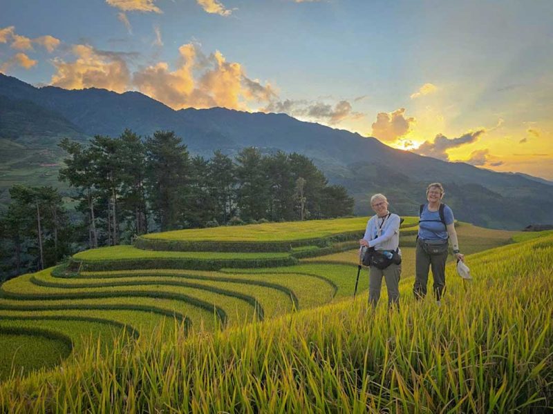 Mu Cang Chai trekking tour with hikers standing among terraced rice fields during a colorful sunset