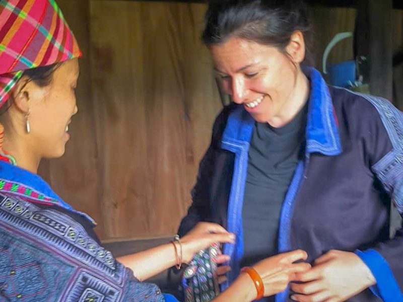 Mu Cang Chai cultural tour homestay activity with a Hmong woman helping a traveler wear traditional clothing