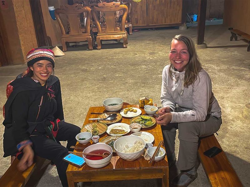 A foreign girl is having a family dinner with local ethnic Red Dao woman in a homestay in Nam Dam Village