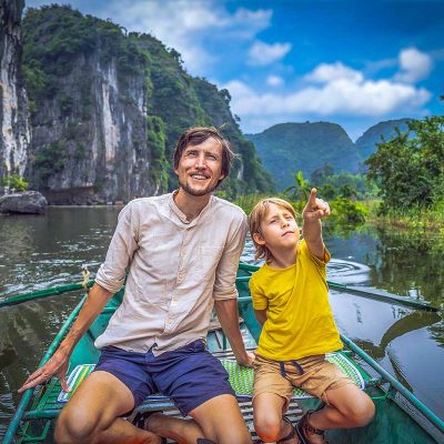 A farther and son sitting in a scenic boat ride in Trang An, one of the best things to do in Ninh Binh with kids