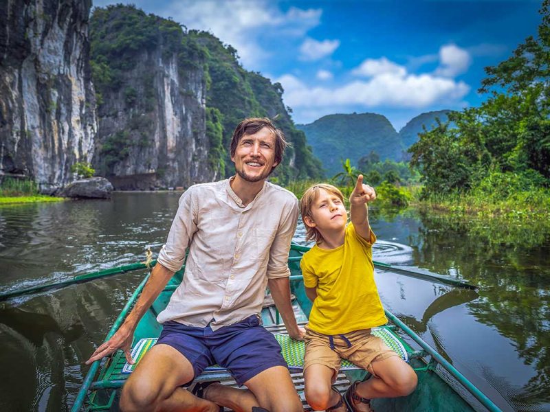 A farther and son sitting in a scenic boat ride in Trang An, one of the best things to do in Ninh Binh with kids