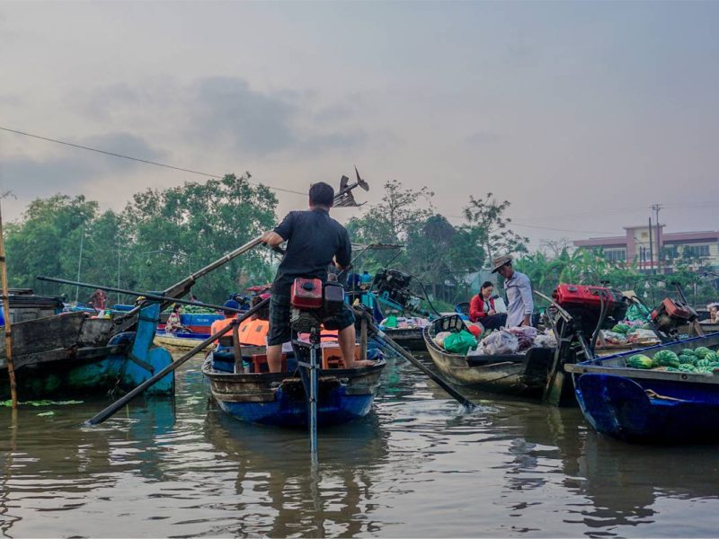 Boatman navigating through Phong Dien Floating Market surrounded by sellers with fruits and vegetables, Can Tho.