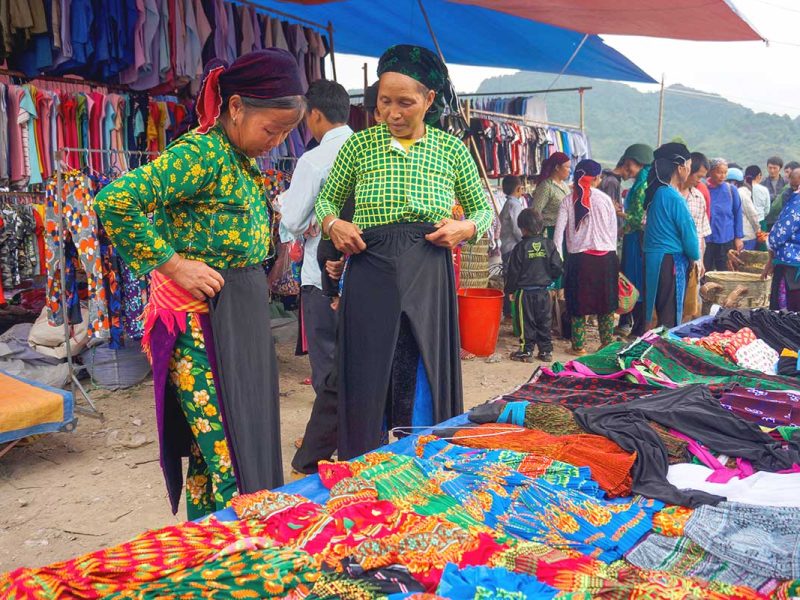 Two colorful ethnic women closely examining goods at the Quan Ba Market in Ha Giang.