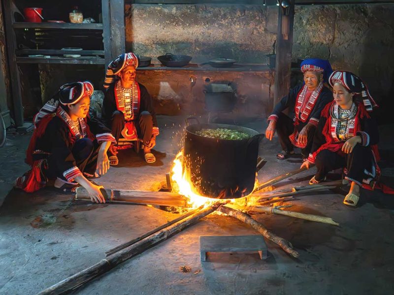 A group of Red Dao woman sitting around a cooking pot on open fire inside the house