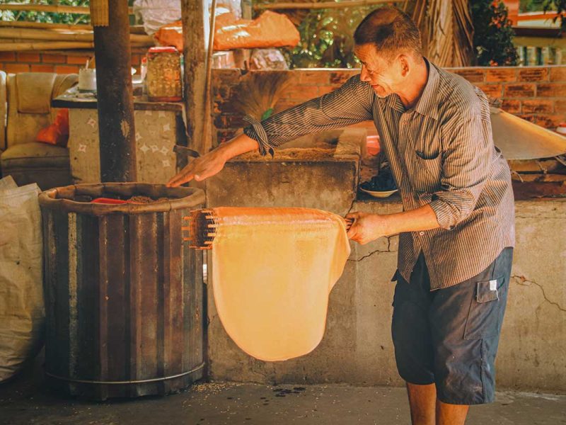 Artisan roasting rice paper over hot coals during production in Can Tho, Vietnam