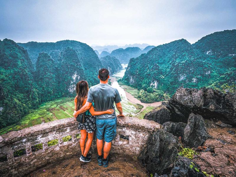 A romantic view of a couple on their honeymoon in Vietnam overlooking the rice fields from Mua Cave at sunset in Ninh Binh