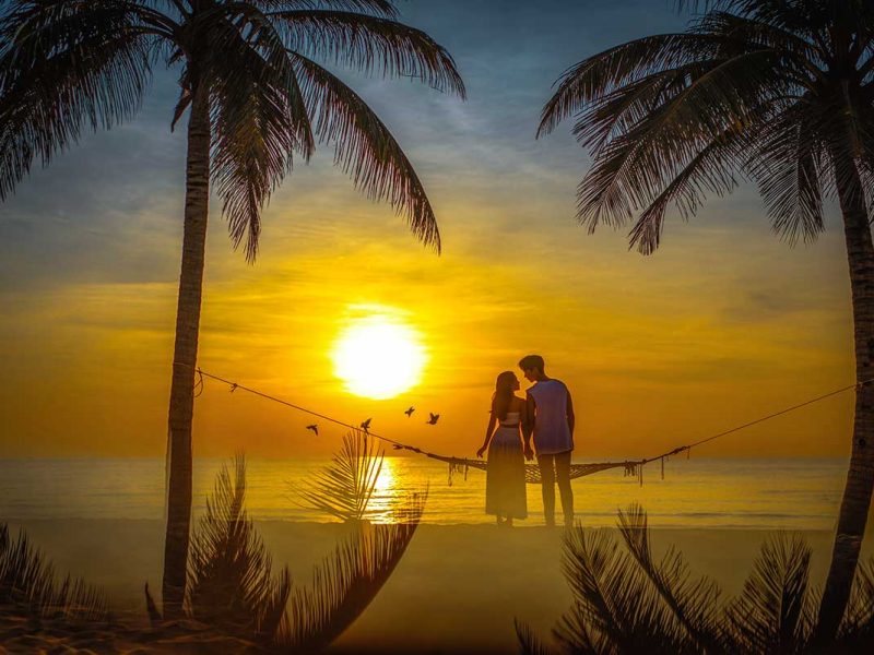 A romantic couple sitting on a hammock on the beach of Phu Quoc while watching the sunset