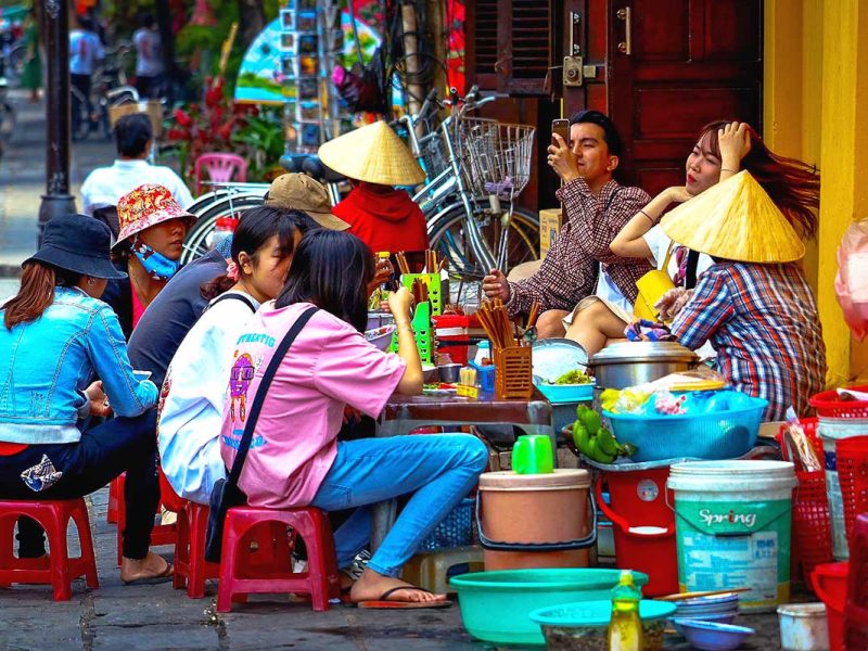 Locals in Hanoi sitting on the street on low plastic stools enjoying local street food.