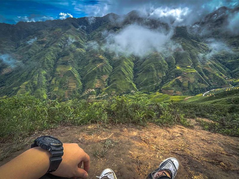 Two feet from a man sitting down with views of the mountain of Ta Xua during a trekking