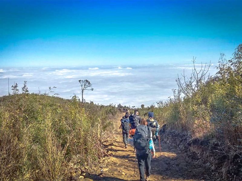 A group of travellers trekking in Ta Xua over a dirt path with on the background below them a sea of clouds