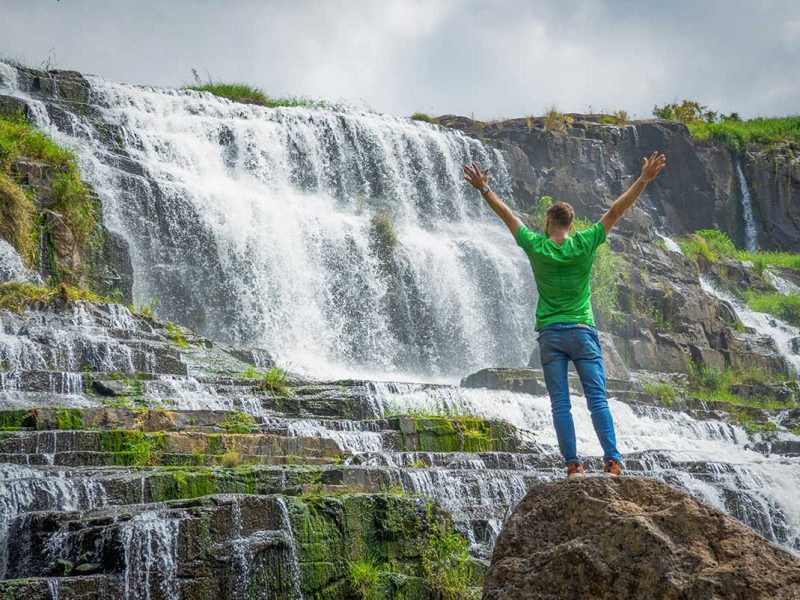 tourist pongour waterfall dalat 1 Traveler standing in front of Pongour Waterfall near Dalat, highlighting the scale of the cascading falls during a Dalat sightseeing tour.