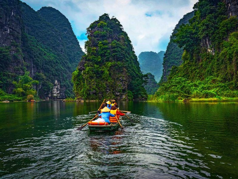 a rowing boat going over the river between high karst mountains in Trang An, Ninh Binh