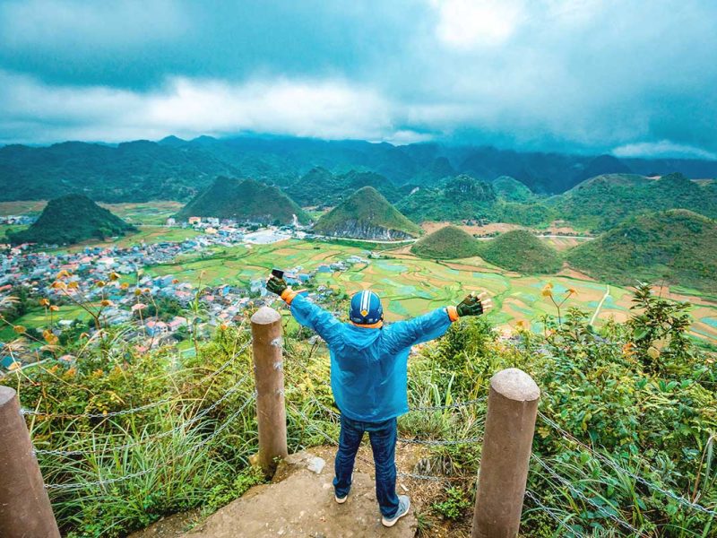 A man standing with arms raised in excitement at the viewpoint overlooking the Twin Mountains in Quan Ba.