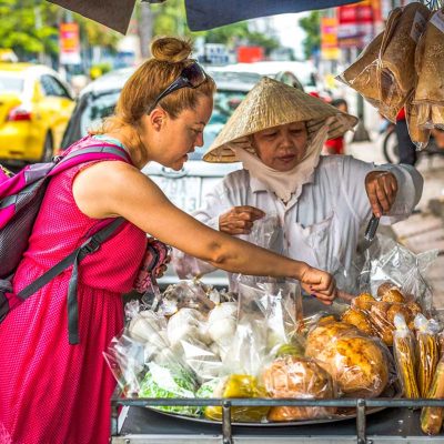 Solo female traveler at a bustling street food vendor in Hanoi, pointing to her food choice.