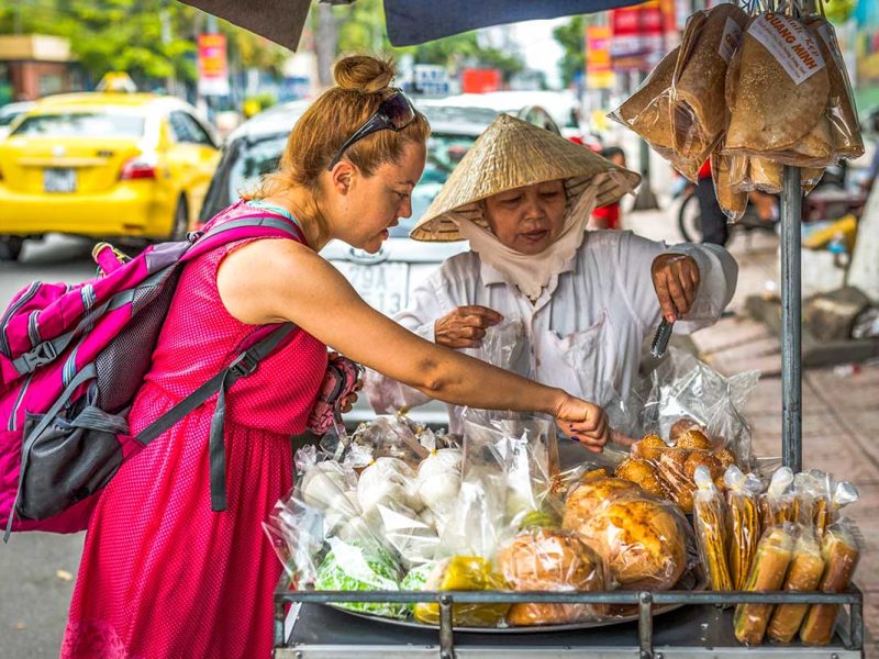 Solo female traveler at a bustling street food vendor in Hanoi, pointing to her food choice.