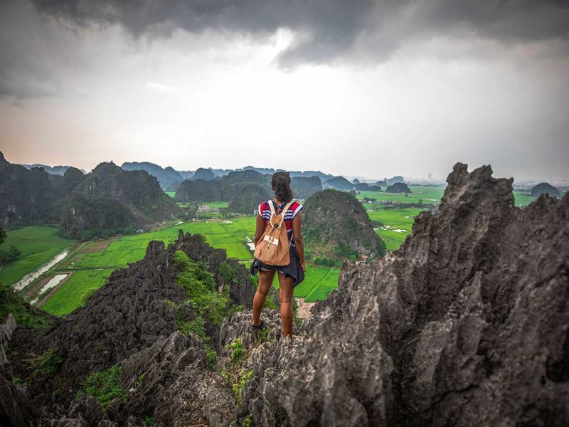 Solo female traveler standing on the rocks at Mua Cave viewpoint, overlooking the scenic landscape of Ninh Binh, Vietnam