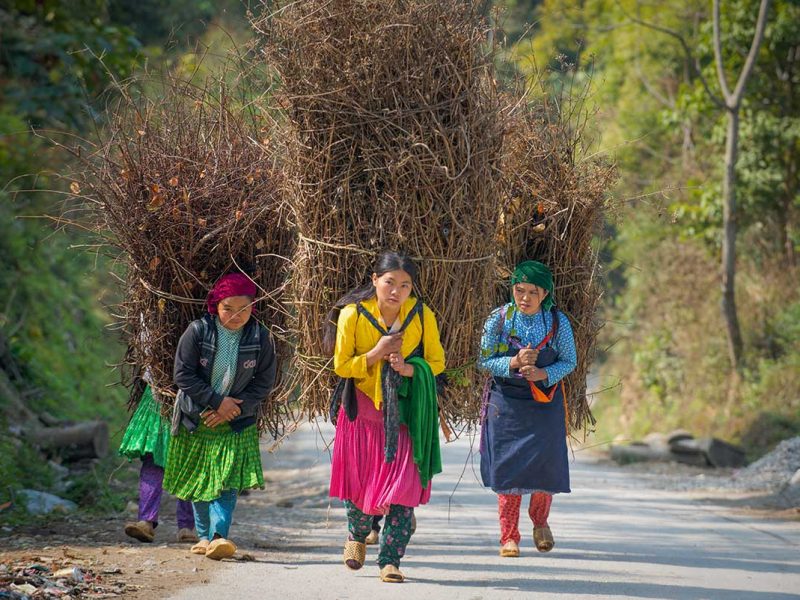 Ethnic women walking along a mountain road surrounded by limestone peaks on the Ha Giang Loop, a popular route for adventurous Vietnam tours.